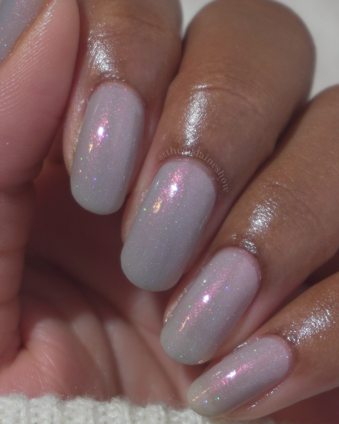 A close-up of a hand with soft grey painted nails against a light background.