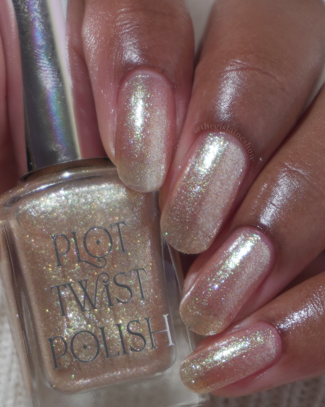 A manicured hand wearing a champagne gold nail polish holding a nail polish bottle.