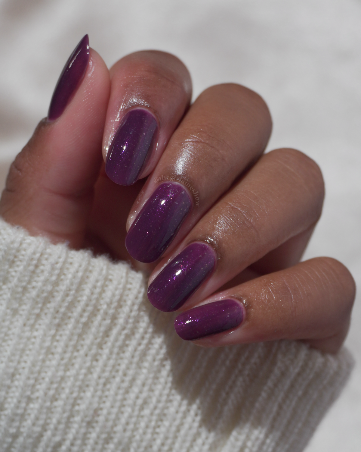 A manicured hand with a dark purple polish with purple shimmer and small gold flakes