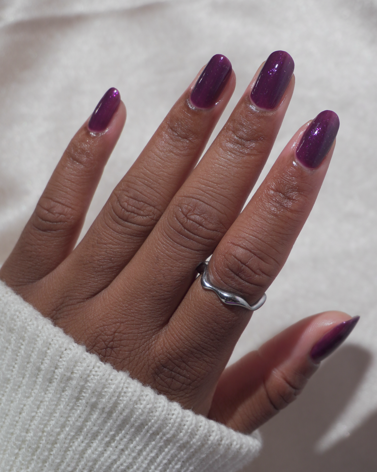 A manicured hand with a dark purple polish with purple shimmer and small gold flakes