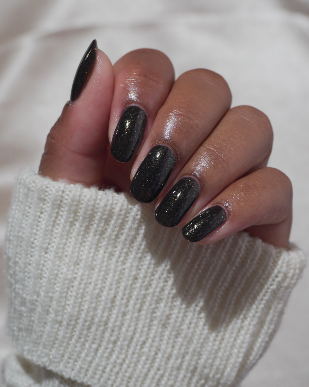 A manicured hand with a black polish with gold flakes.