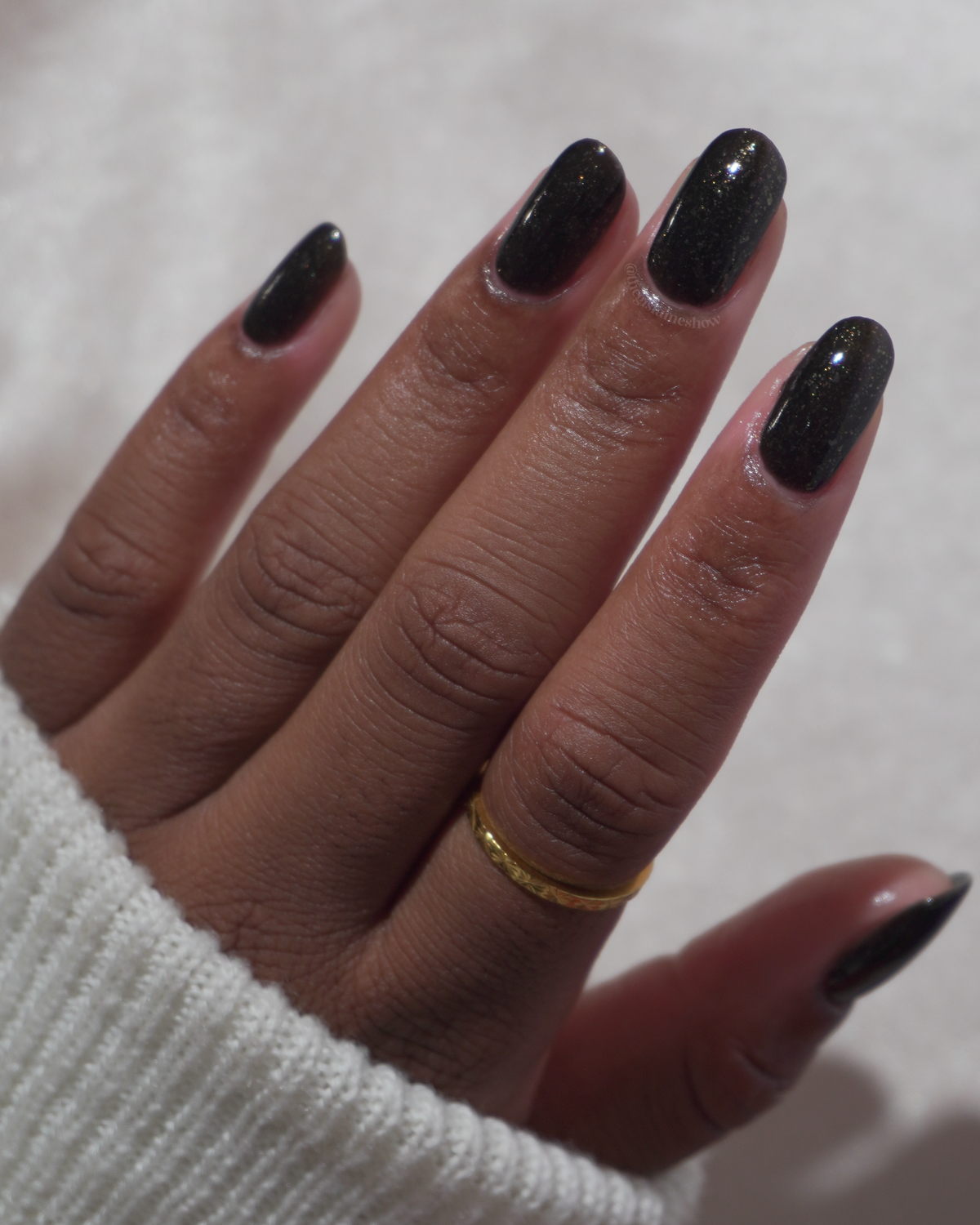 A manicured hand with a black polish with gold flakes.