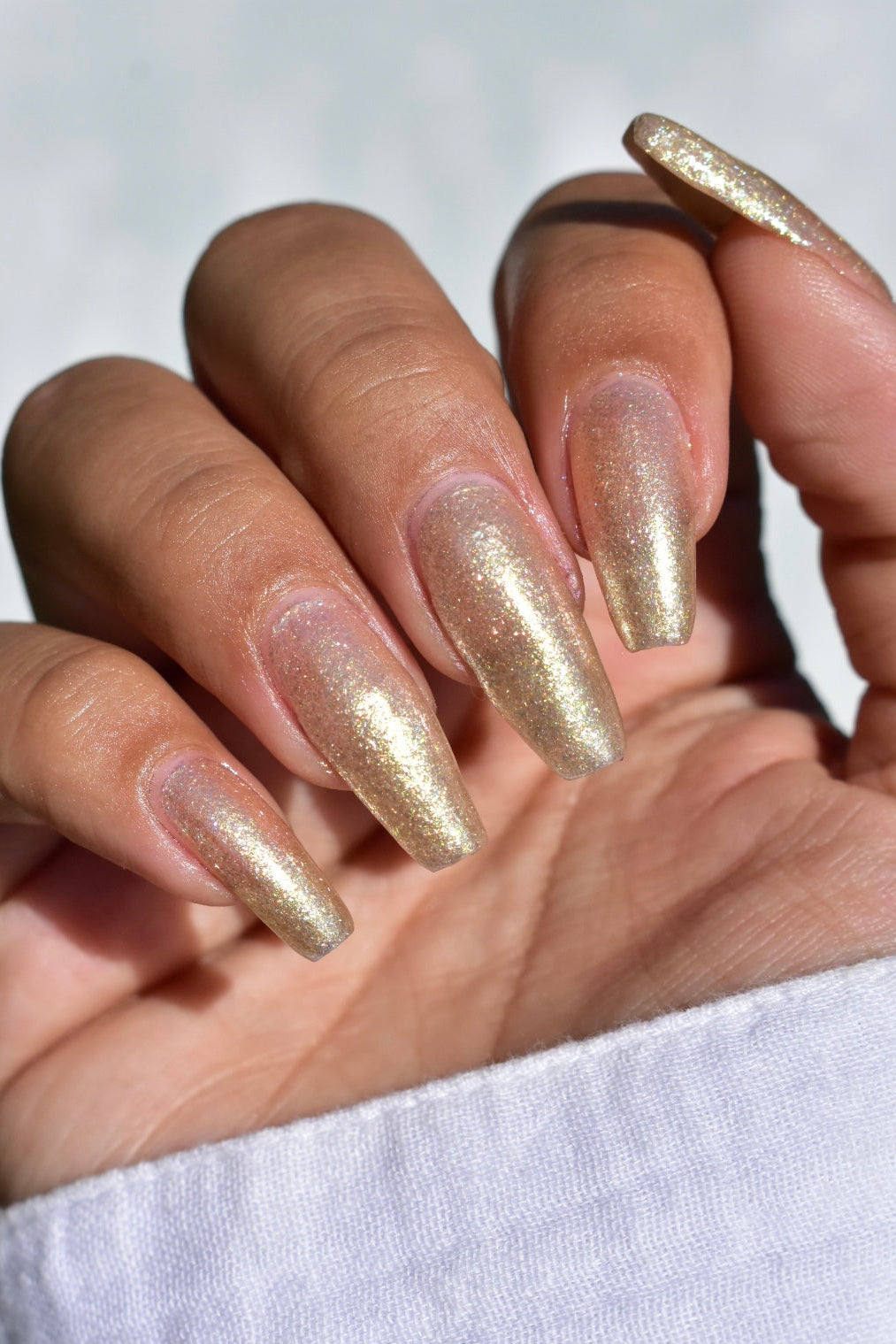 A manicured hand wearing a champagne gold nail polish.