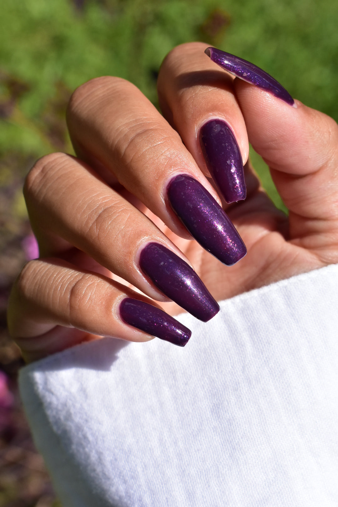 A manicured hand with a dark purple polish with purple shimmer and small gold flakes