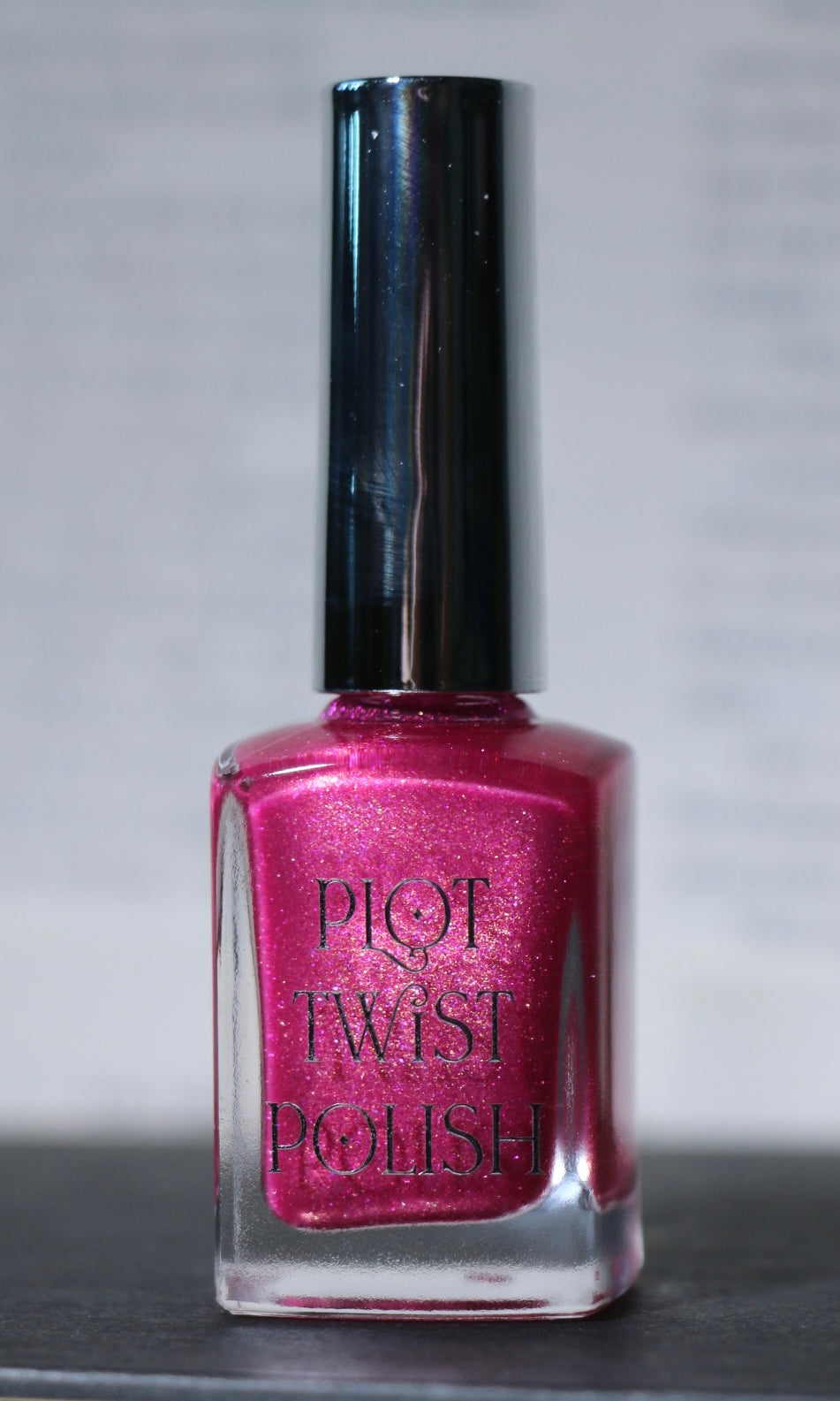 A bottle of Plot Twist Polish nail lacquer in a shimmering magenta-pink shade, featuring a glossy silver cap and clear glass bottle.