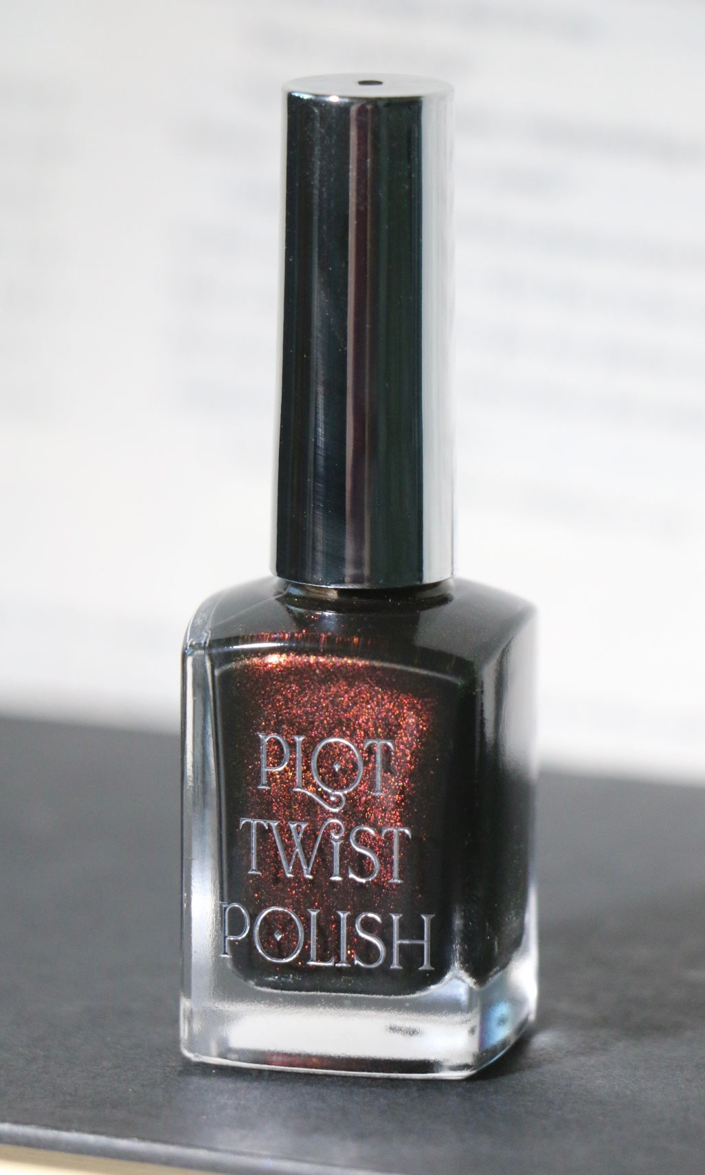 A bottle of Plot Twist Polish nail lacquer with a metallic copper-brown glitter polish, featuring a reflective silver cap, set against a neutral gray and white background.