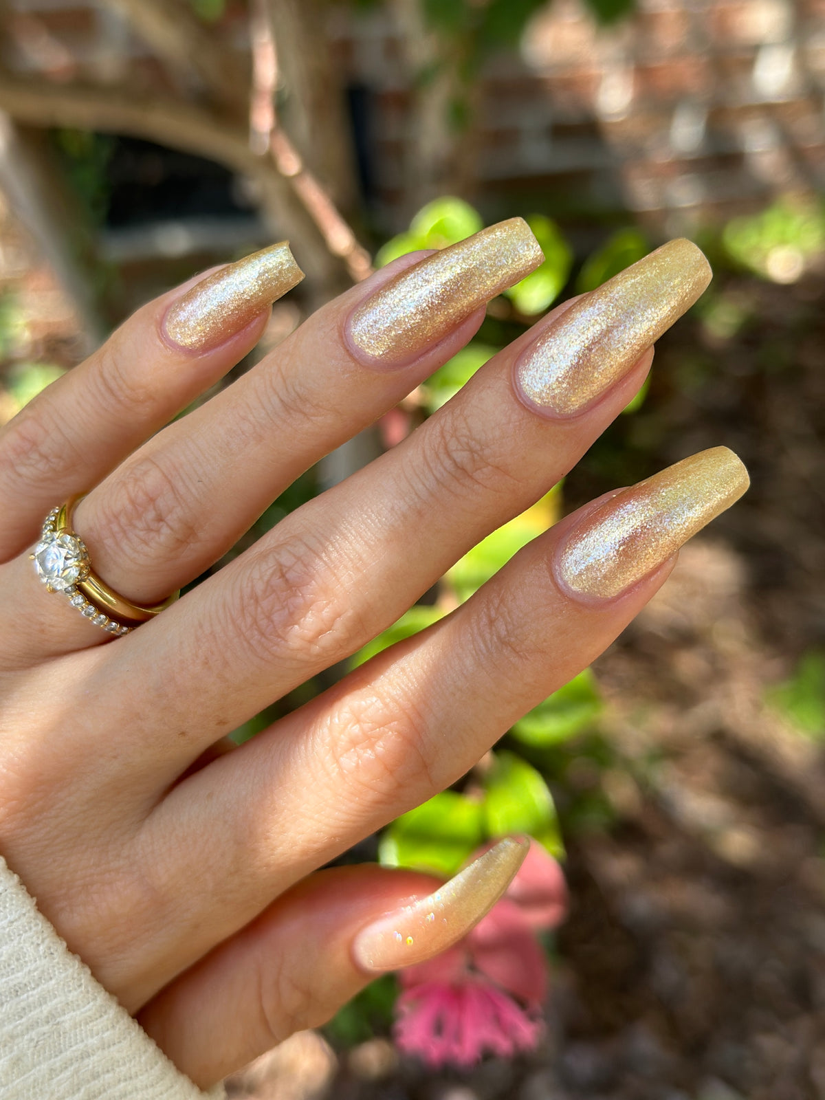 A manicured hand wearing a champagne gold nail polish.