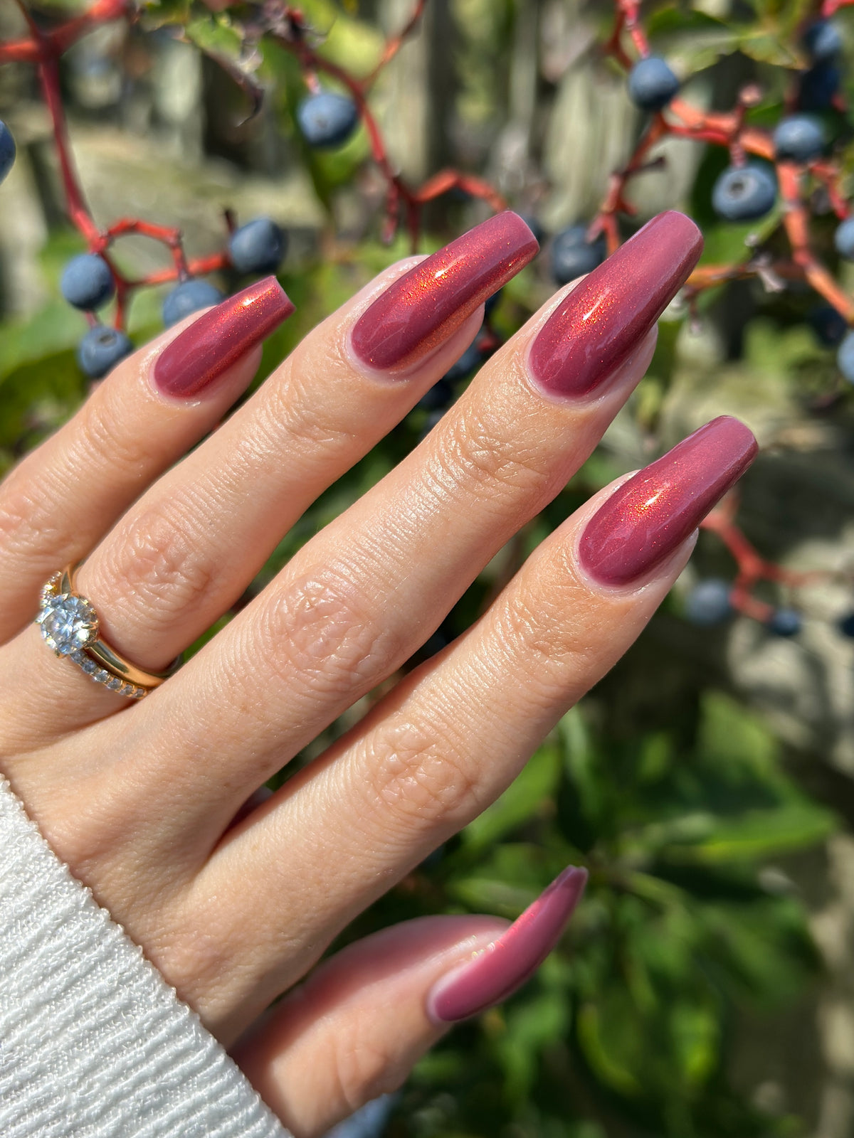 A hand with a manicure of a rose polish with a red to orange shimmer glow.