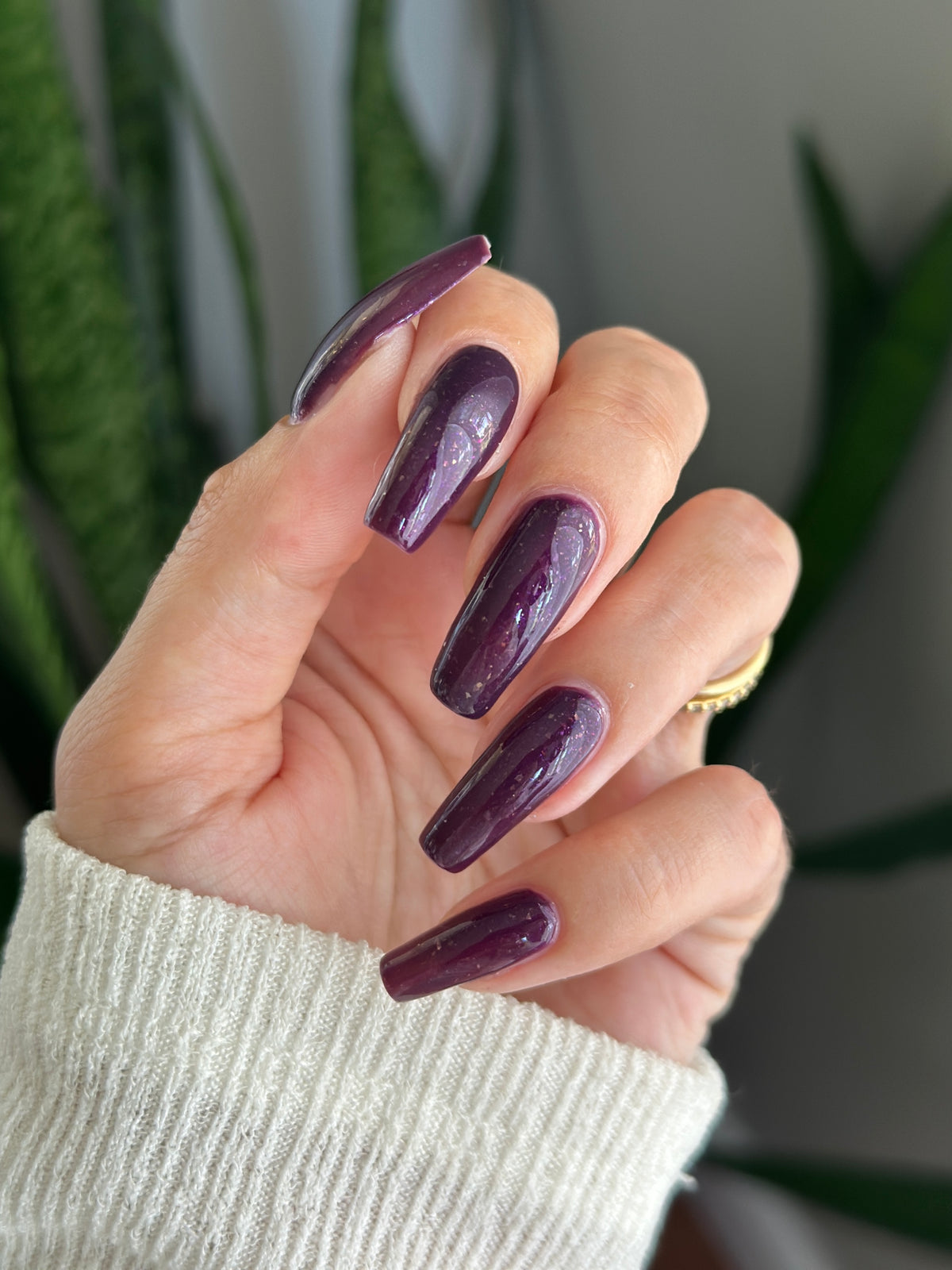 A manicured hand with a dark purple polish with purple shimmer and small gold flakes.