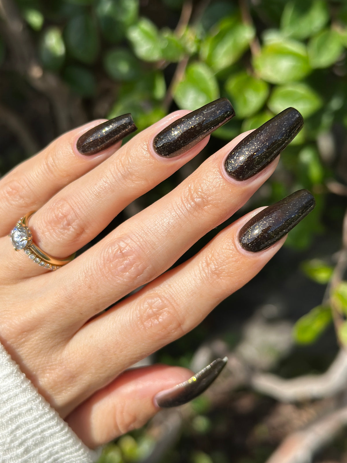 A manicured hand with a black polish with gold flakes.