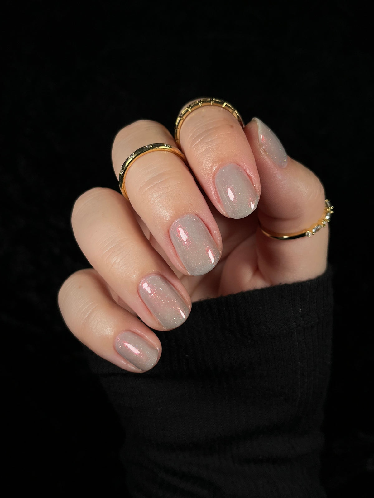 A close-up of a hand with soft grey painted nails against a black background.