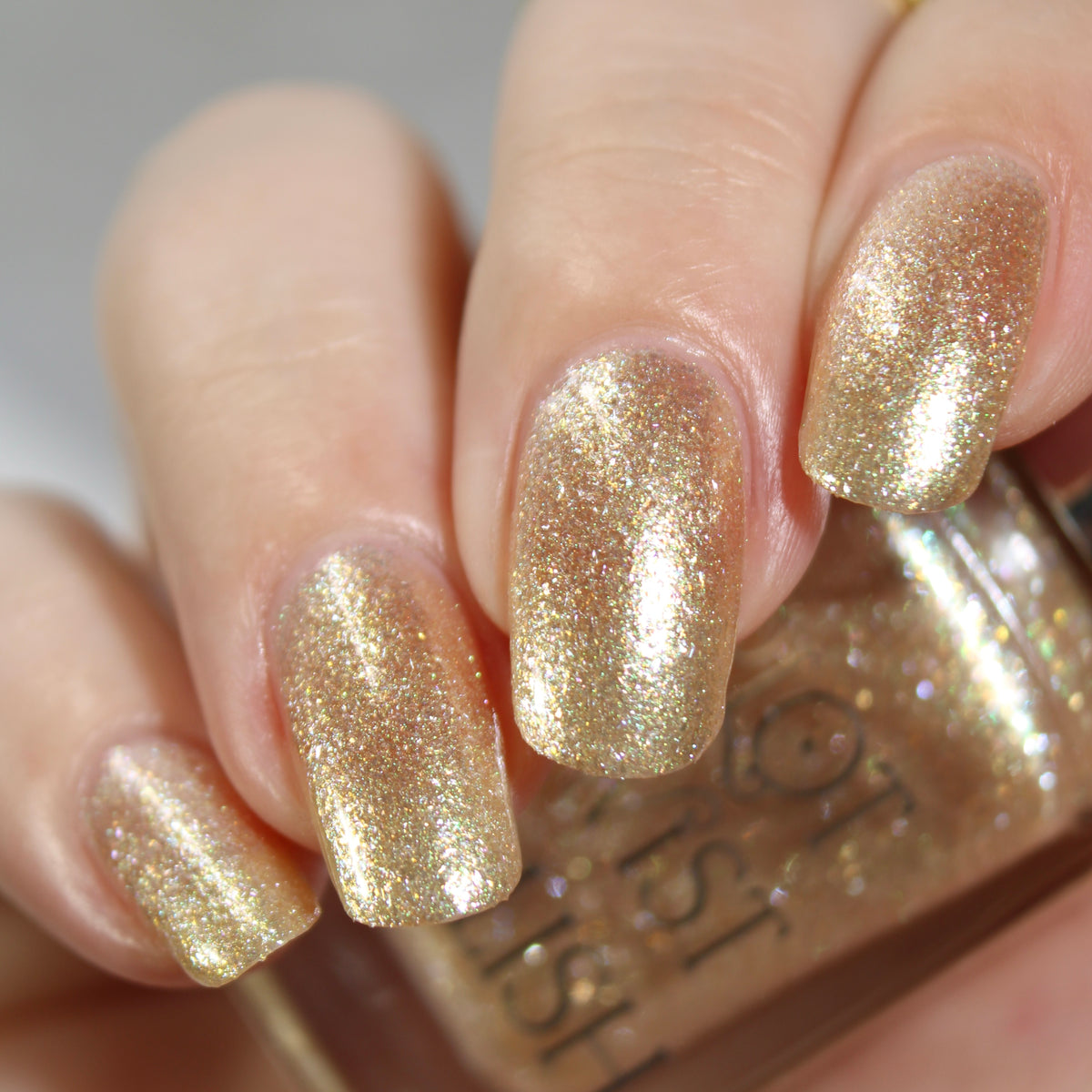 A manicured hand wearing a champagne gold nail polish holding a nail polish bottle