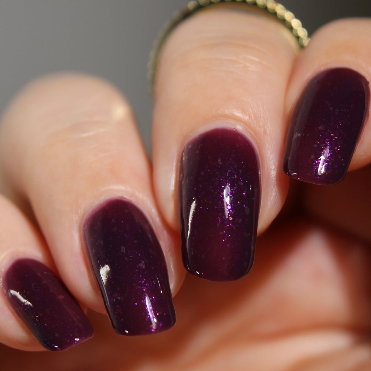 A manicured hand with a dark purple polish with purple shimmer and small gold flakes