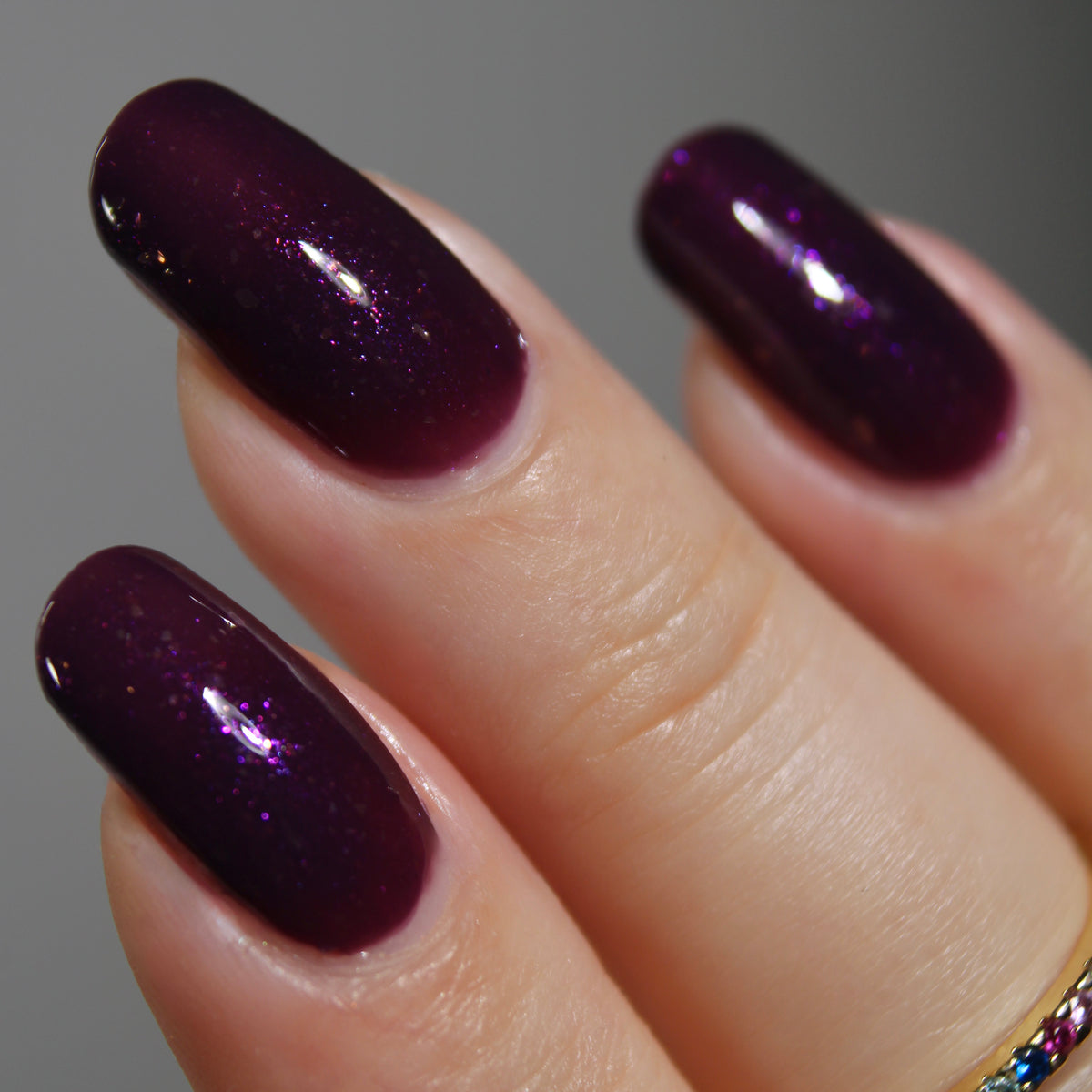 A manicured hand with a dark purple polish with purple shimmer and small gold flakes