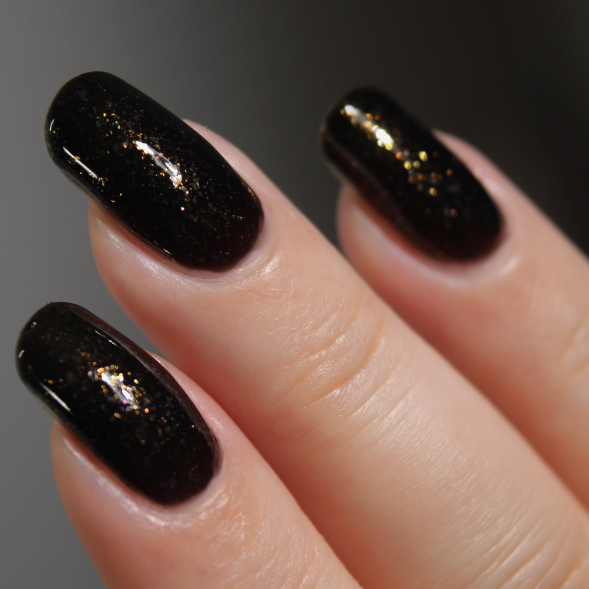 A manicured hand with a black polish with gold flakes.