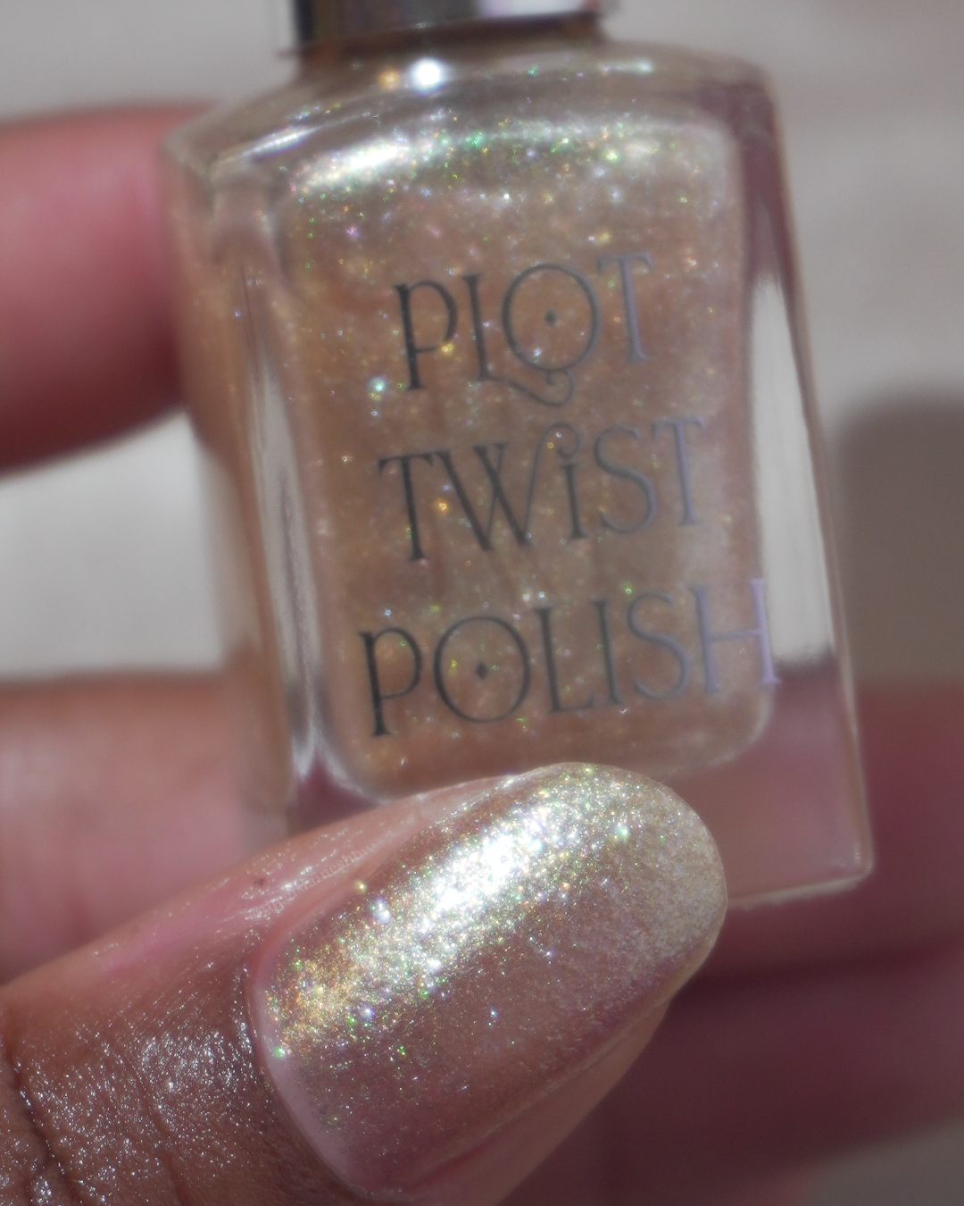A close up photo of a thumb wearing a gold polish and holding a nail polish bottle.