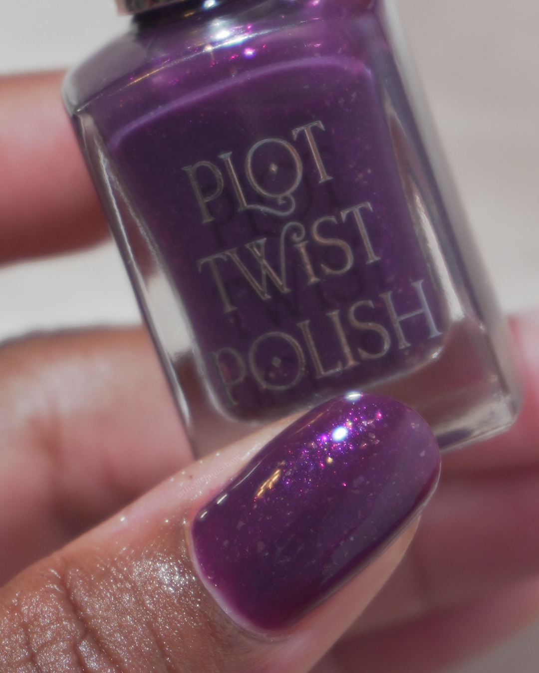 A close up photo of a thumb wearing a purple polish and holding a nail polish bottle.