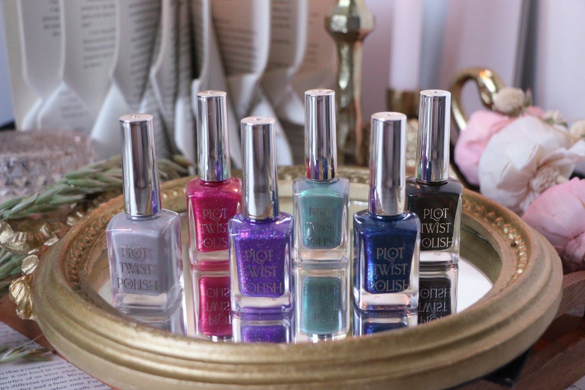 Six bottles of Plot Twist Polish nail polish in various colors, arranged on a round gold tray with a reflective surface.