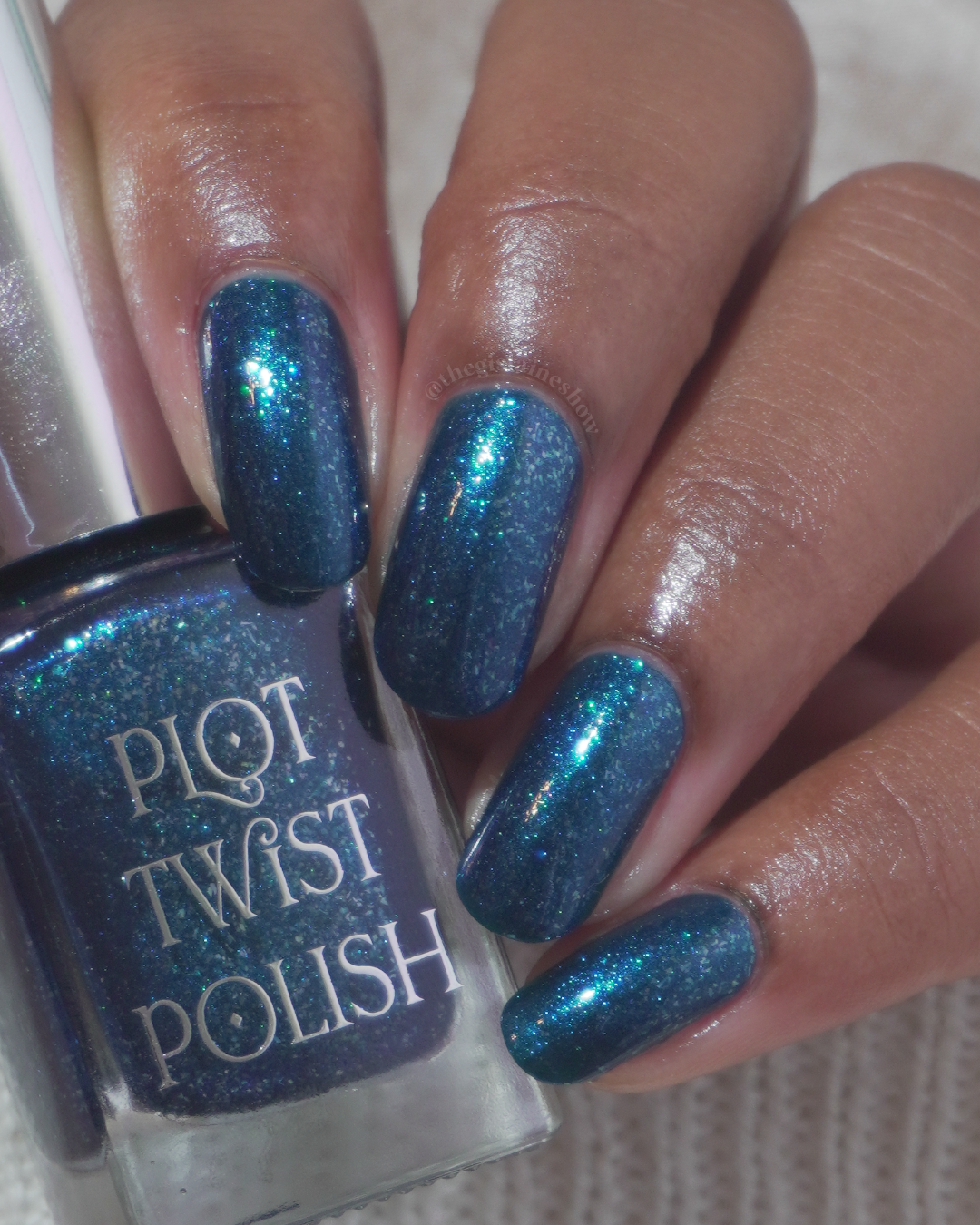 A close-up of a hand with nails painted in a sparkling teal-blue nail polish, holding a bottle labeled 'PLOT TWIST POLISH'.