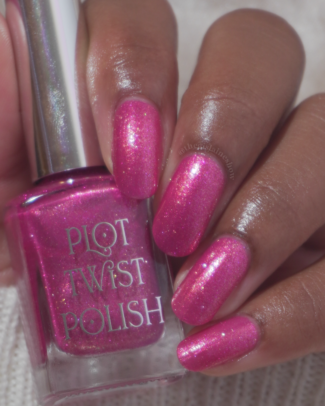 A close-up of a hand with long, glossy pink glitter nail polish swatches next to a bottle of Plot Twist Polish in the matching bright pink shade.