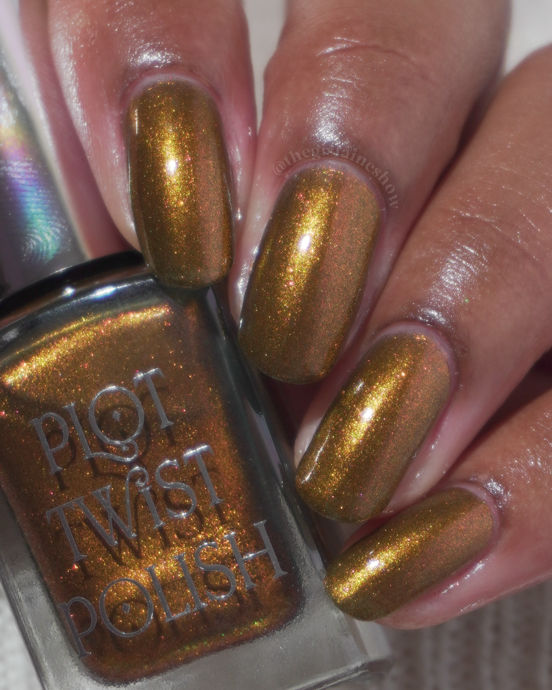 A hand with a copper shimmer manicure holding a bottle of nail polish. 
