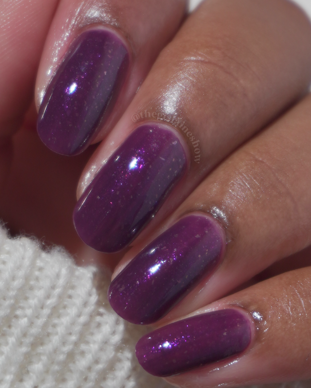 A manicured hand with a dark purple polish with purple shimmer and small gold flakes