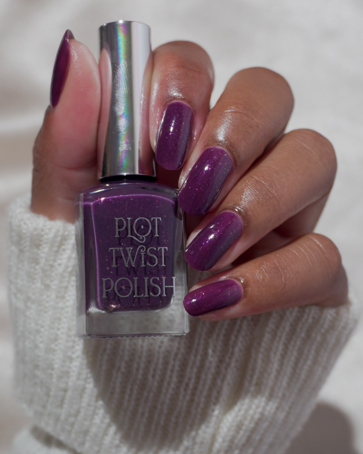 A manicured hand wearing a purple polish holding a bottle of nail polish