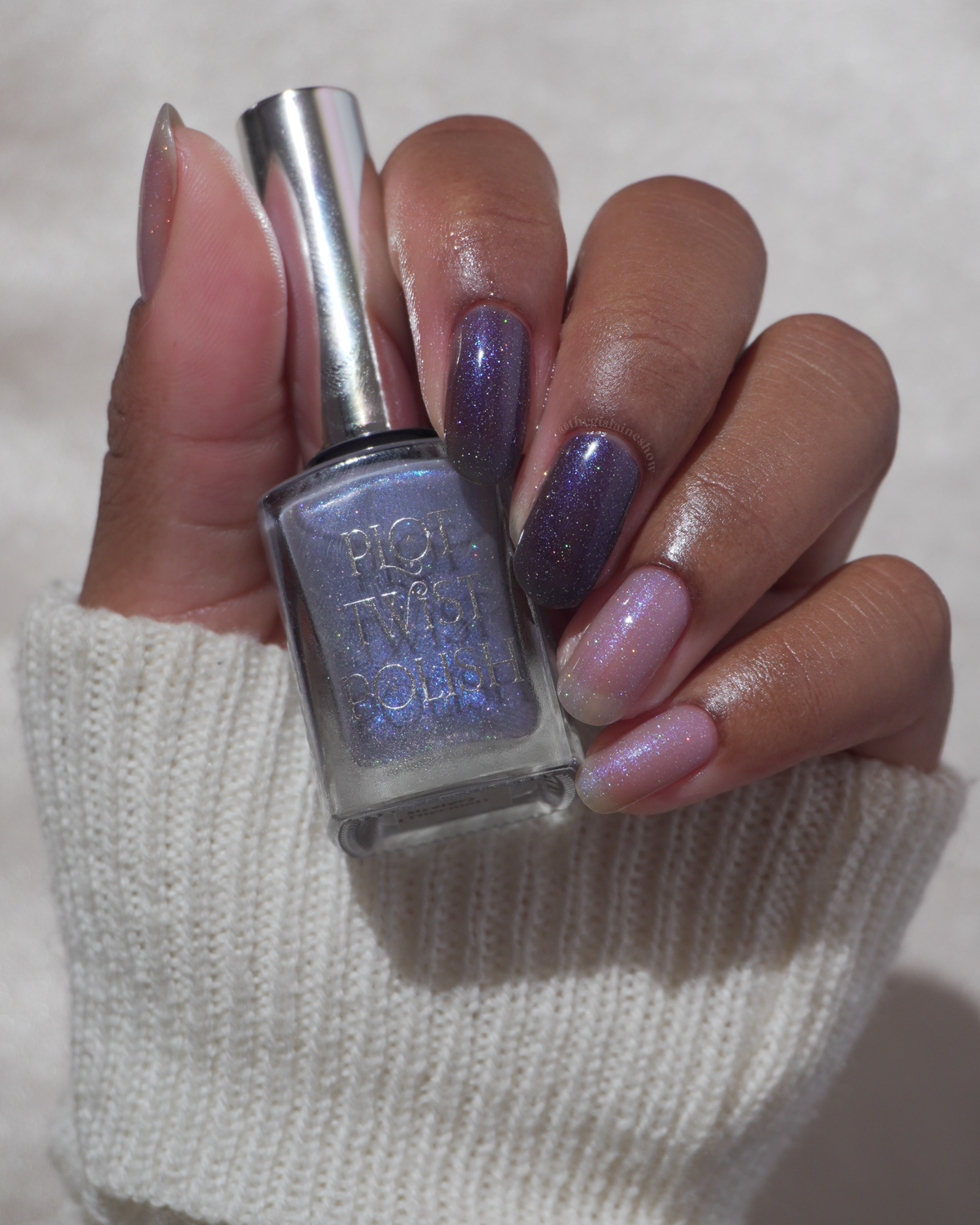 A manicured hand with 2 fingers in a  translucent shimmery nail polish and 2 fingers in a blue polish, holding a nail polish bottle.