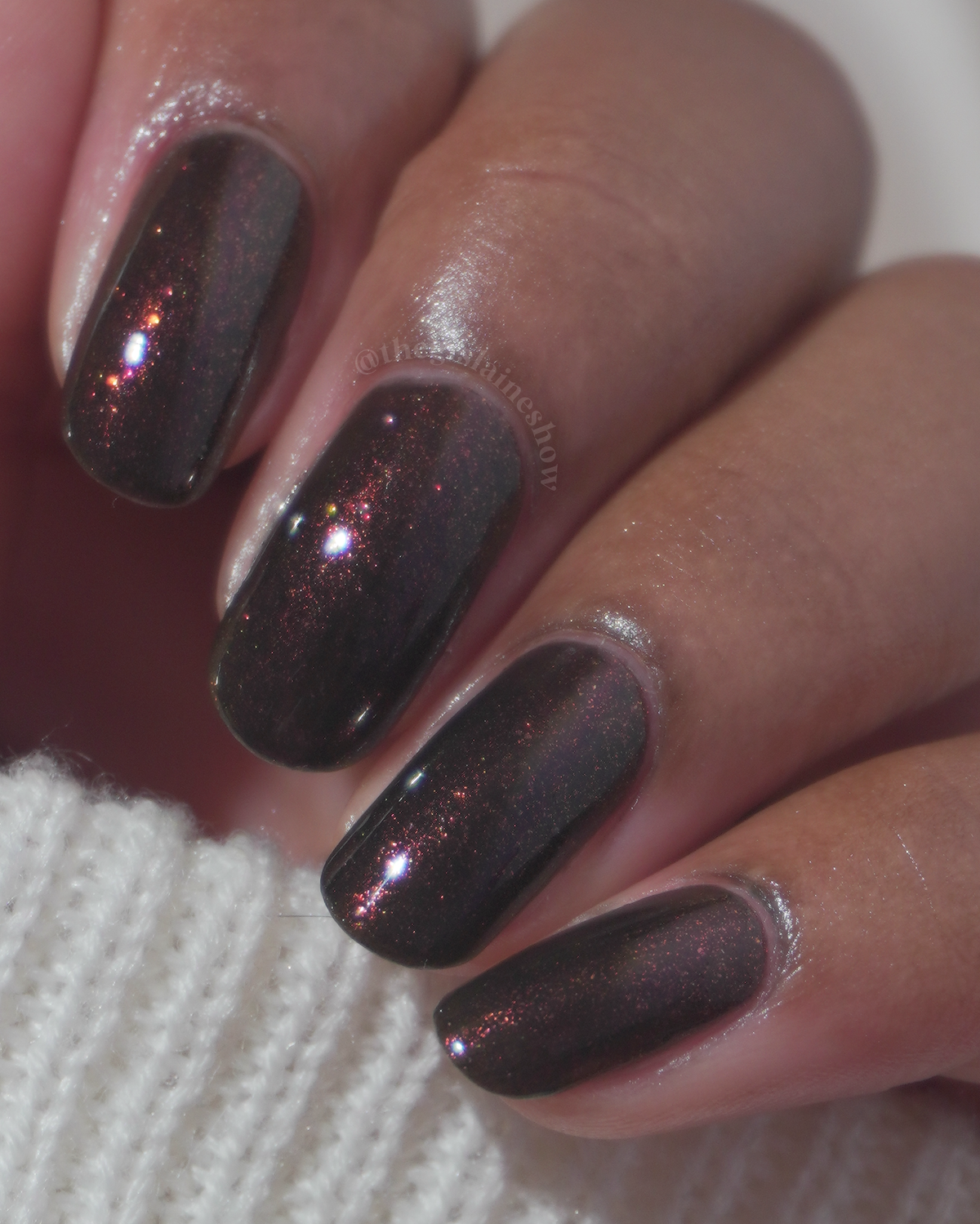 Close-up of a hand with manicured nails painted in a dark metallic brown polish.