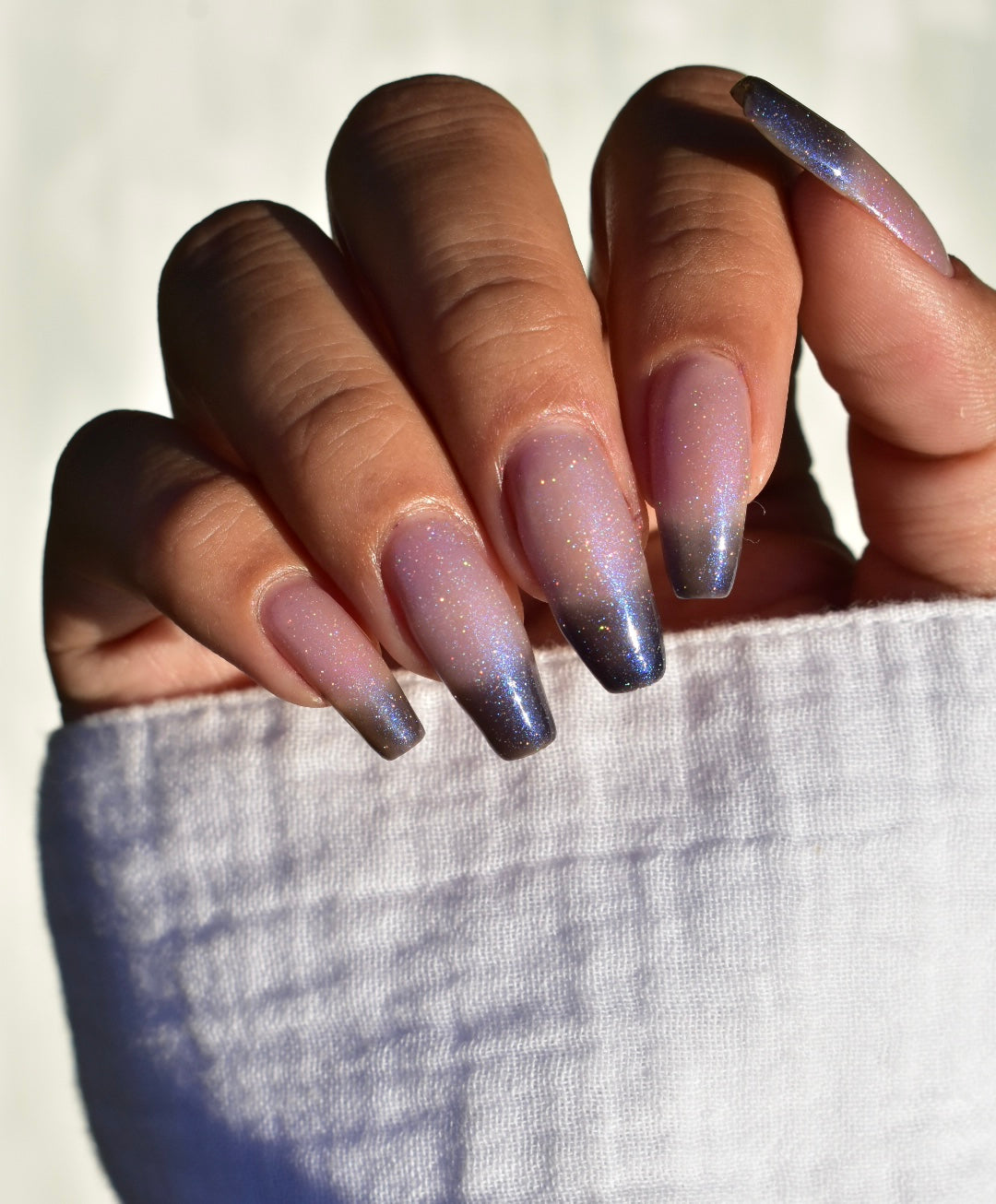 A manicured hand with a translucent shimmery nail polish base and blue nail tips.