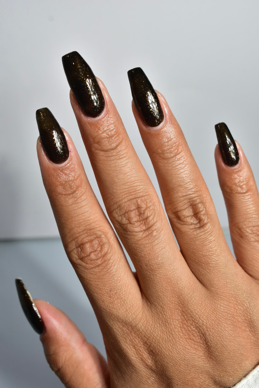 A manicured hand of a black polish with gold flakes. 