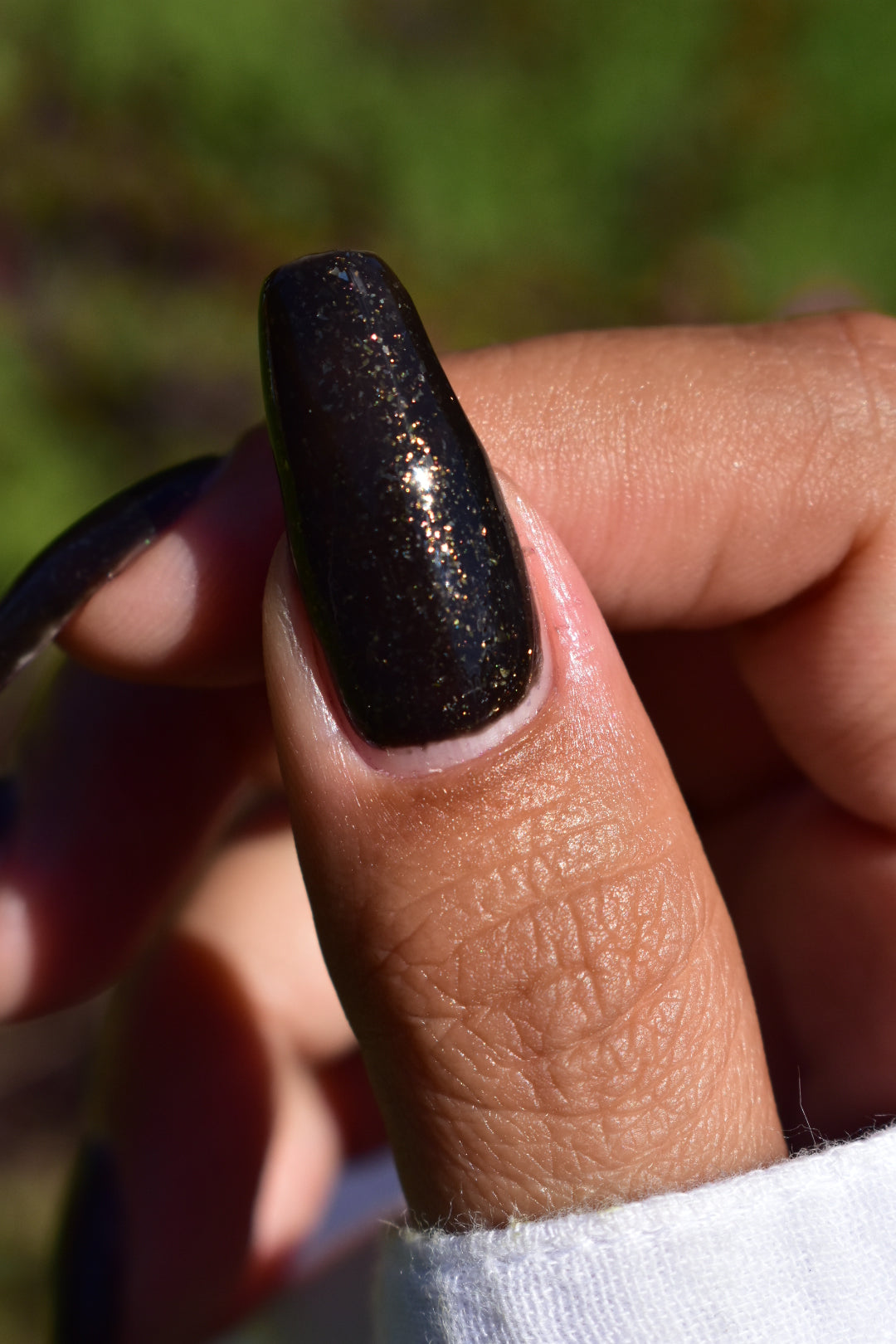 A manicured thumb with a black polish with gold flakes. 