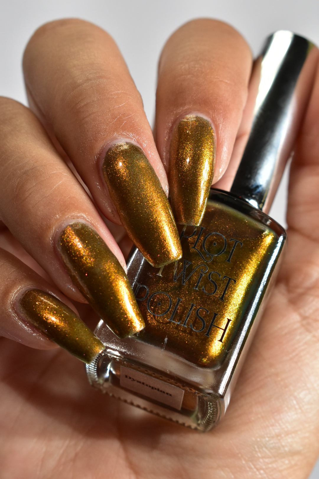 A hand with a copper shimmer manicure holding a nail polish bottle. 