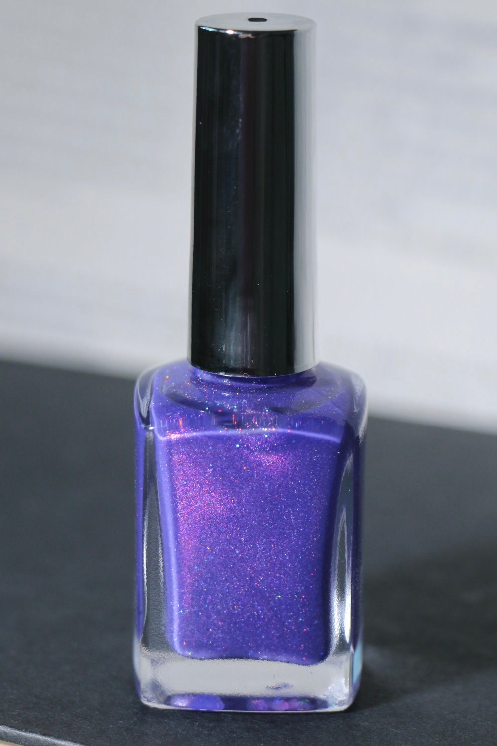 A bottle of Plot Twist Polish nail lacquer in a shimmering purple shade, featuring a silver cap and silver lettering on the clear glass bottle.