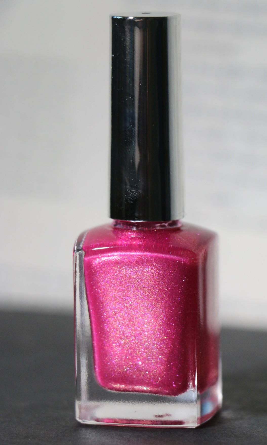 A bottle of Plot Twist Polish nail lacquer in a shimmering magenta-pink shade, featuring a glossy silver cap and clear glass bottle.