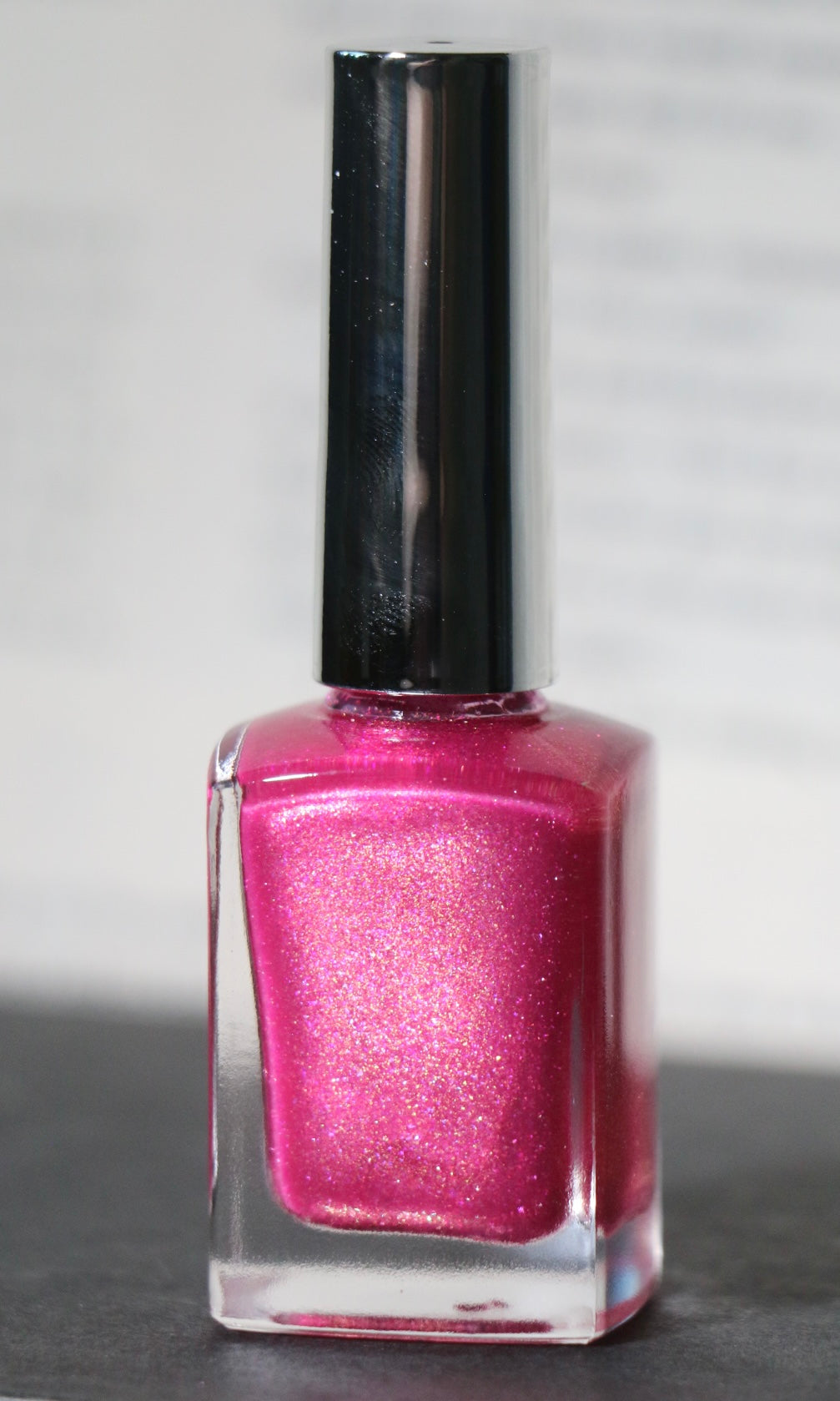 A bottle of Plot Twist Polish nail lacquer in a shimmering magenta-pink shade, featuring a glossy silver cap and clear glass bottle.
