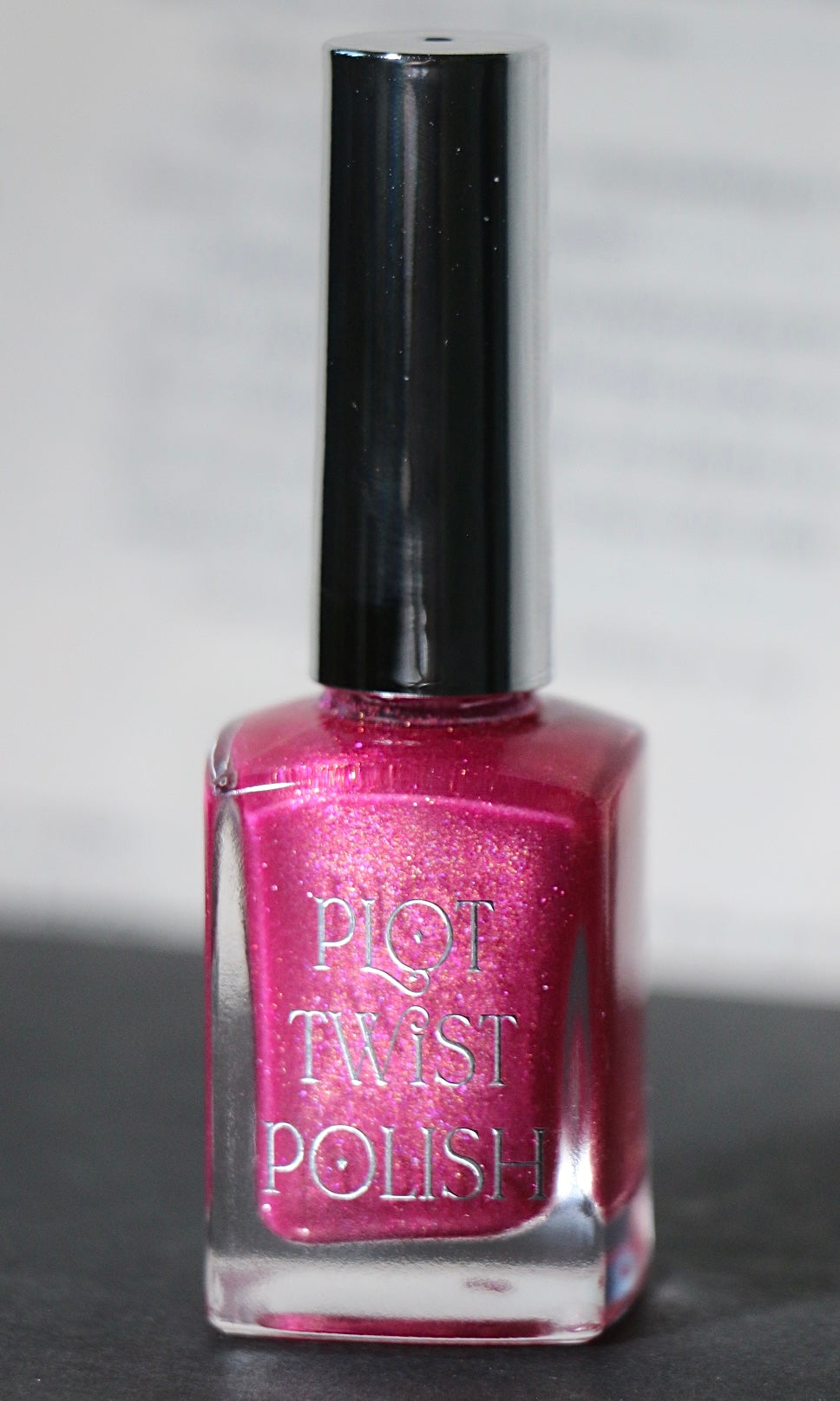 A bottle of Plot Twist Polish nail lacquer in a shimmering magenta-pink shade, featuring a glossy silver cap and clear glass bottle.