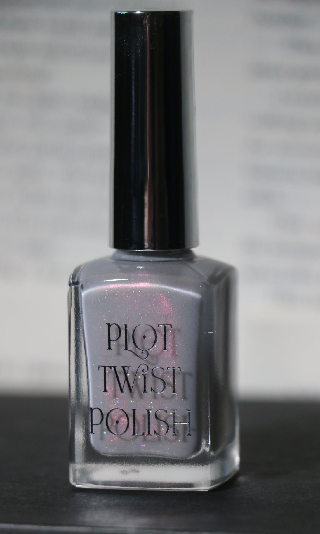 A bottle of Plot Twist nail polish in a shimmering light silver-gray shade, featuring a silver cap and clear glass bottle with the brand name printed on the front.
