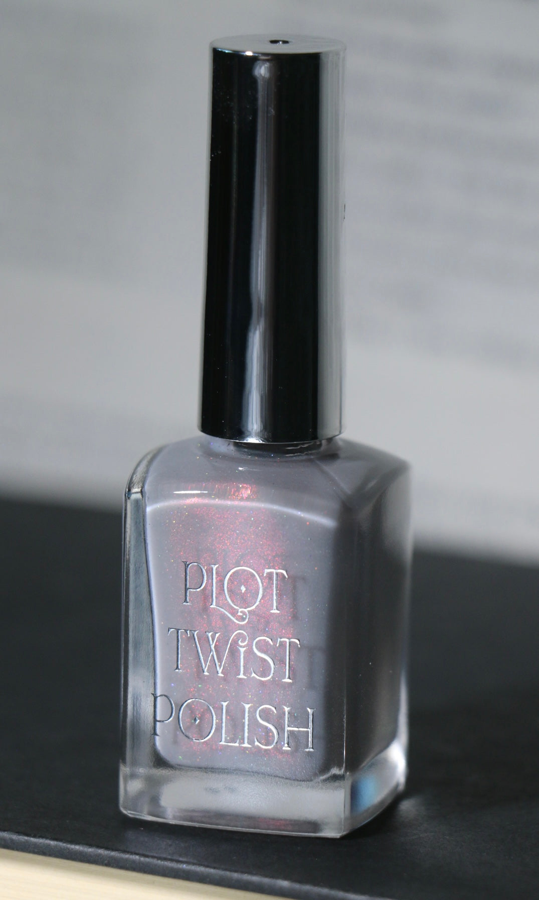 A bottle of Pilot Twist nail polish in a shimmering silver-gray shade, featuring a silver cap and clear glass bottle, set against a dark and light gray background.
