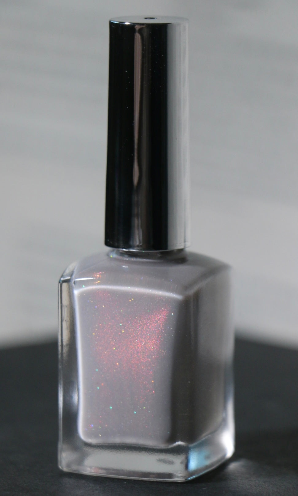 A bottle of silver glitter nail polish with a reflective silver cap, set against a neutral gray background.
