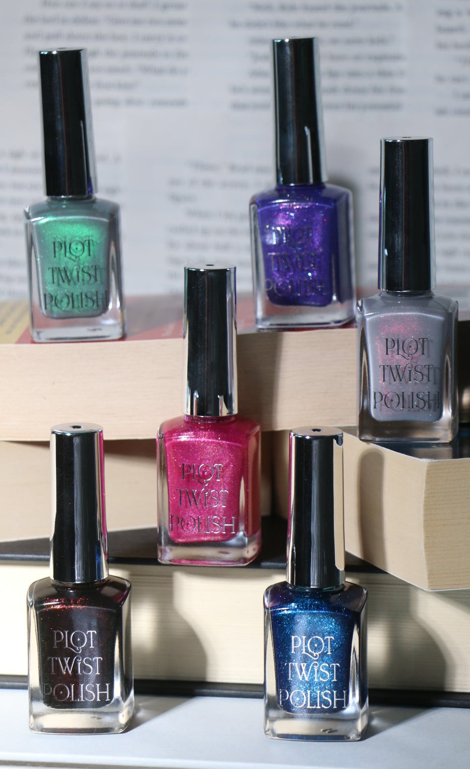 Six bottles of nail polish in pink, purple, green, grey, blue, and black sitting on top of books. 