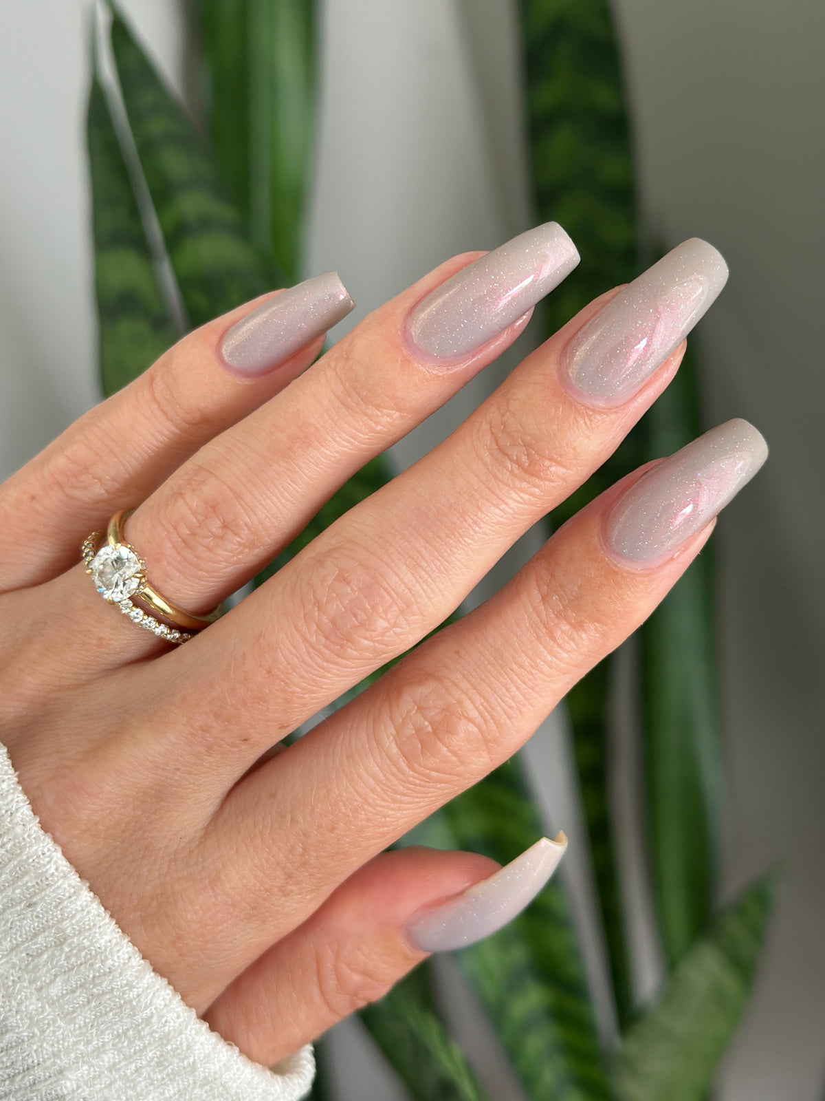A close-up of a hand with long, almond-shaped nails with a light grey nail polish color. 