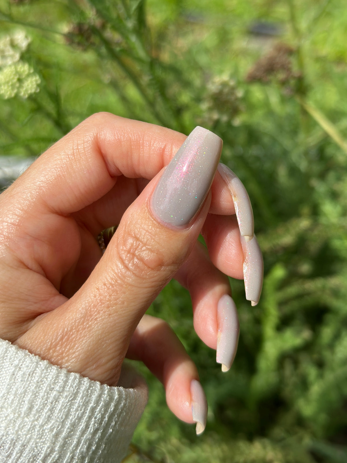 A close-up of a thumb with soft grey painted nails outside.