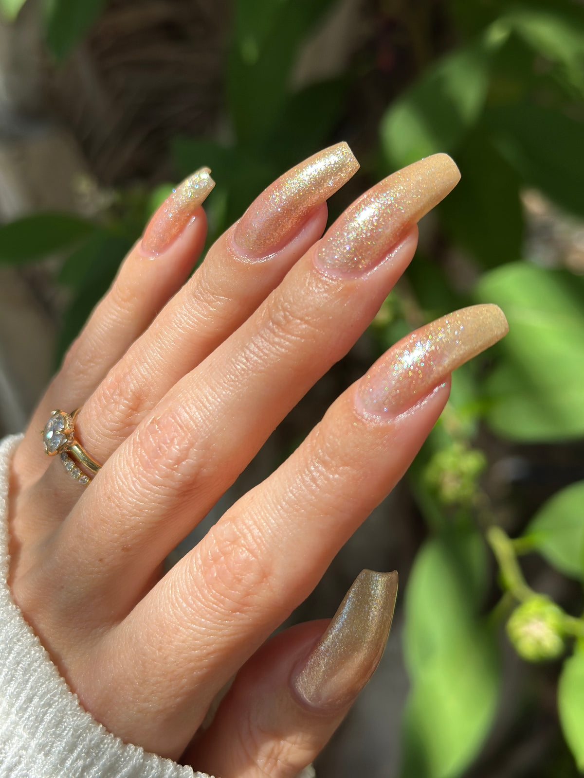 A manicured hand wearing a champagne gold nail polish.