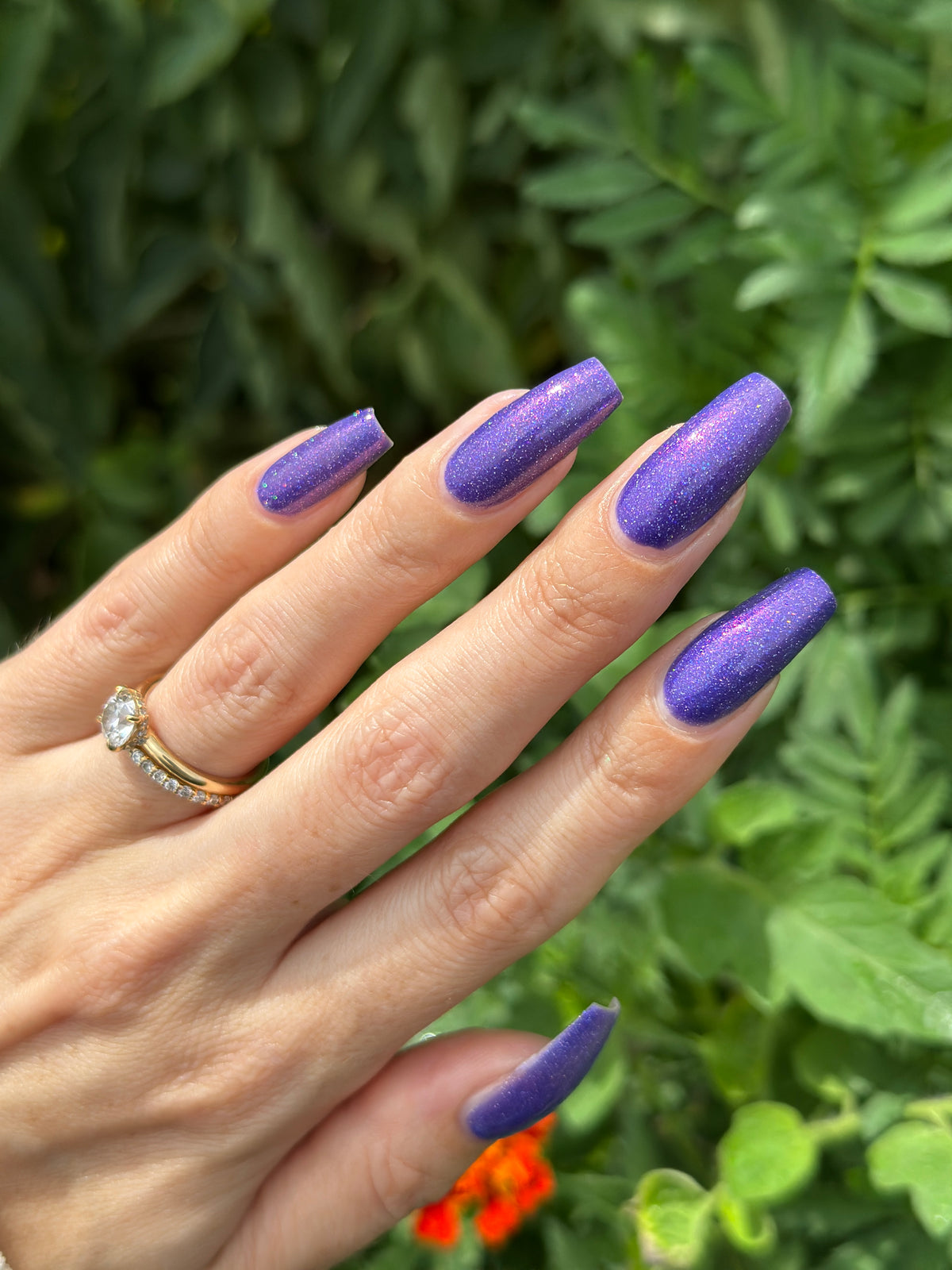 A close-up of a hand with long, square-shaped nails painted in a sparkling purple glitter polish.