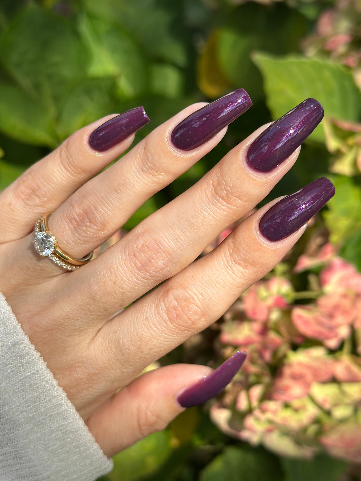 A manicured hand with a dark purple polish with purple shimmer and small gold flakes