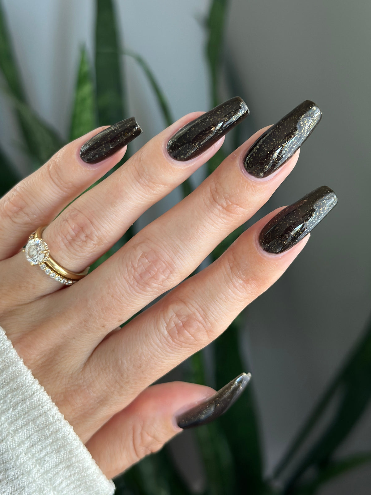 A manicured hand with a black polish with gold flakes. 