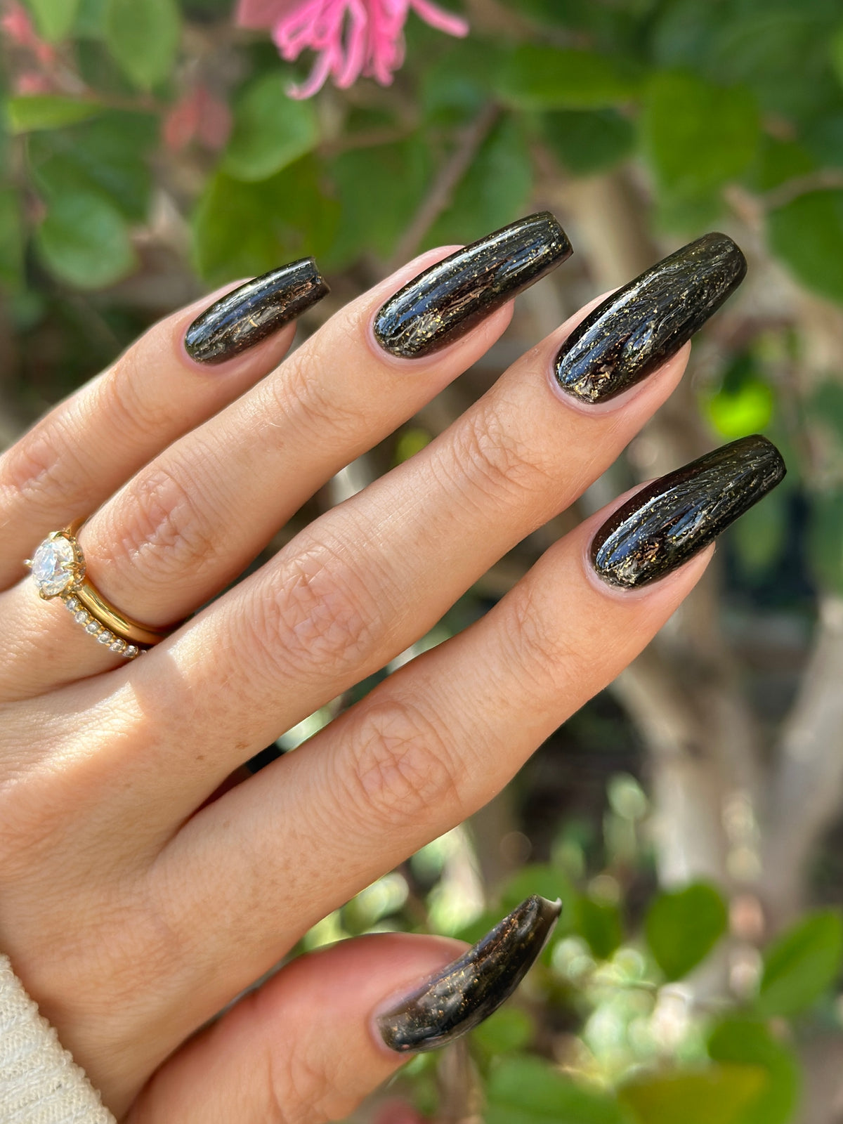 A manicured hand with a black polish with gold flakes. 