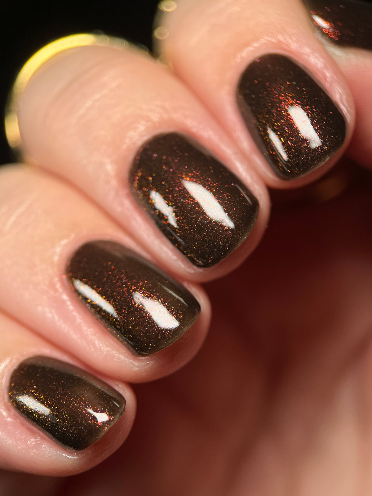 Close-up of fingernails painted with a dark metallic brown polish featuring fine gold shimmer and a subtle reflective sheen.