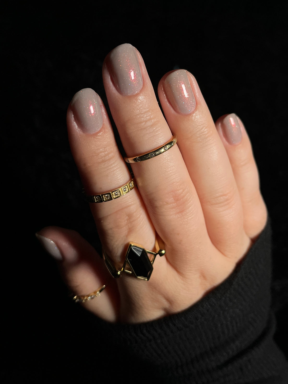 A close-up of a hand with soft grey painted nails against a black background.